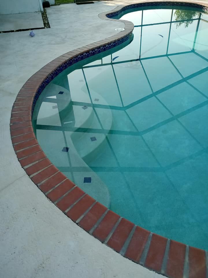 Pool with brick coping and steps, surrounded by a light-colored concrete deck. Water is clear blue.