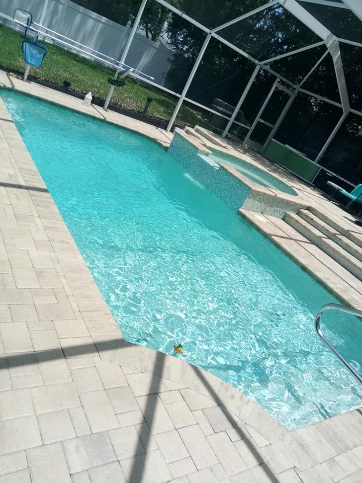 Swimming pool with turquoise water, beige tile deck, and a screened enclosure.