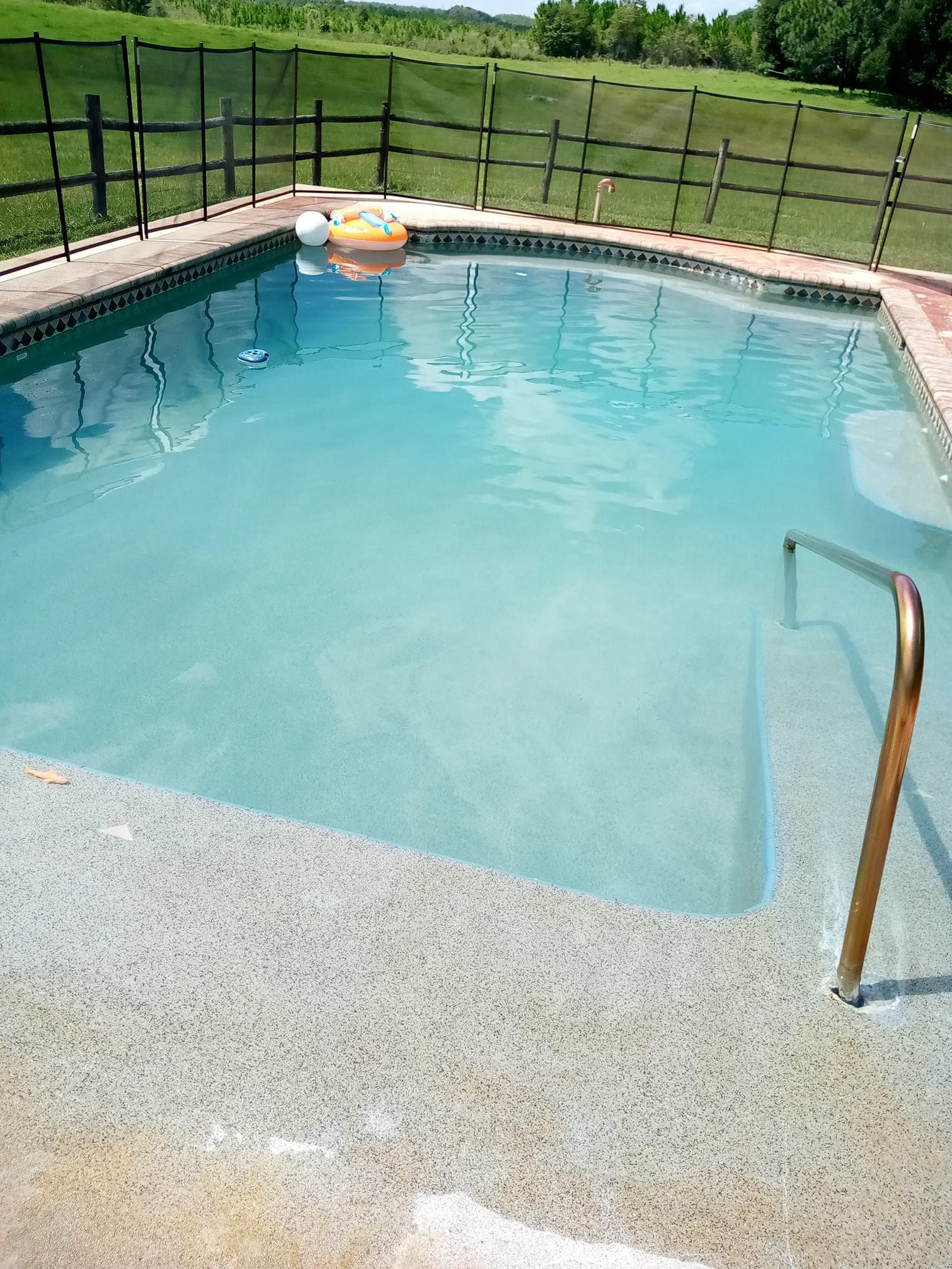 A rectangular swimming pool filled with clear water. It has a built-in step with a metal handrail.