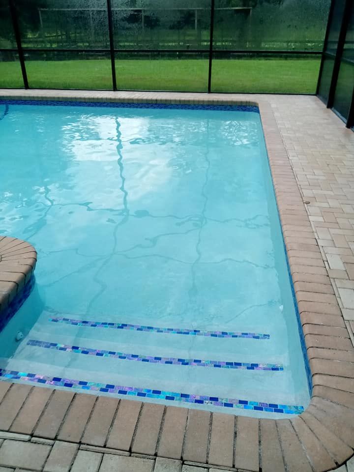 Pool with blue water and steps, surrounded by brick patio. Screened enclosure in background.