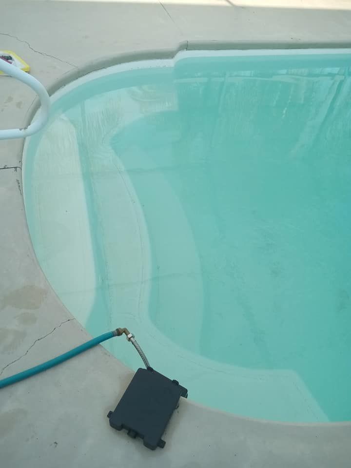 Pool filled with turquoise water, steps, and a blue hose attached to a black box.