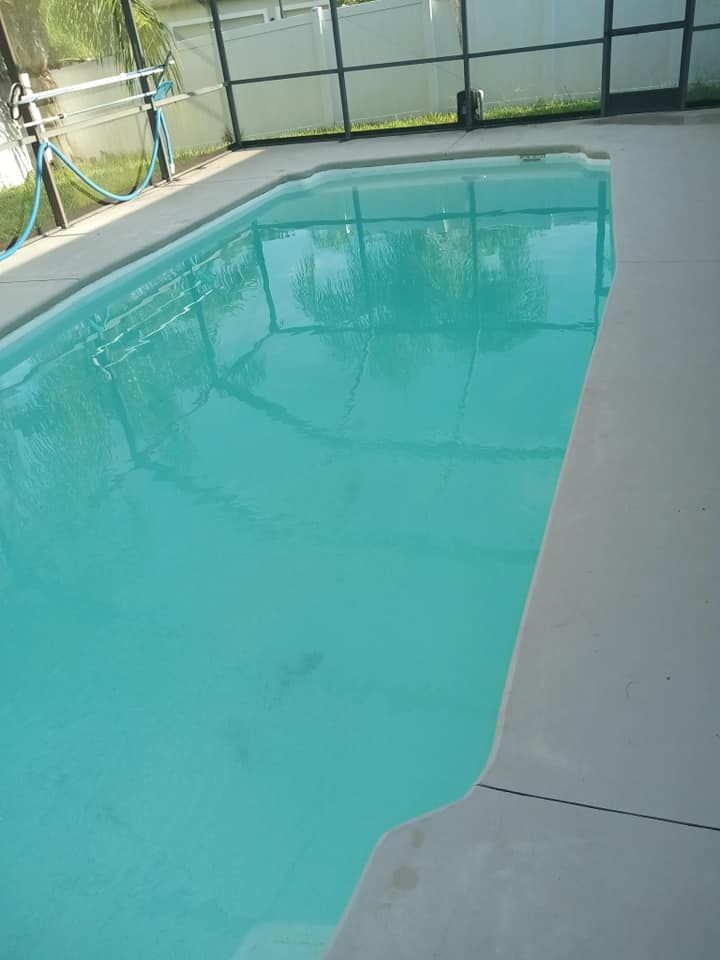 Swimming pool filled with turquoise water, surrounded by concrete deck and screened enclosure.