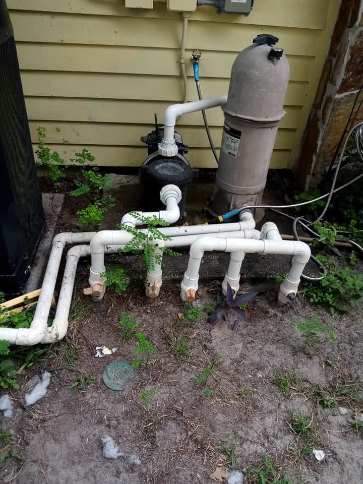 Pool pump and filter system with white PVC pipes, set against a light yellow building.