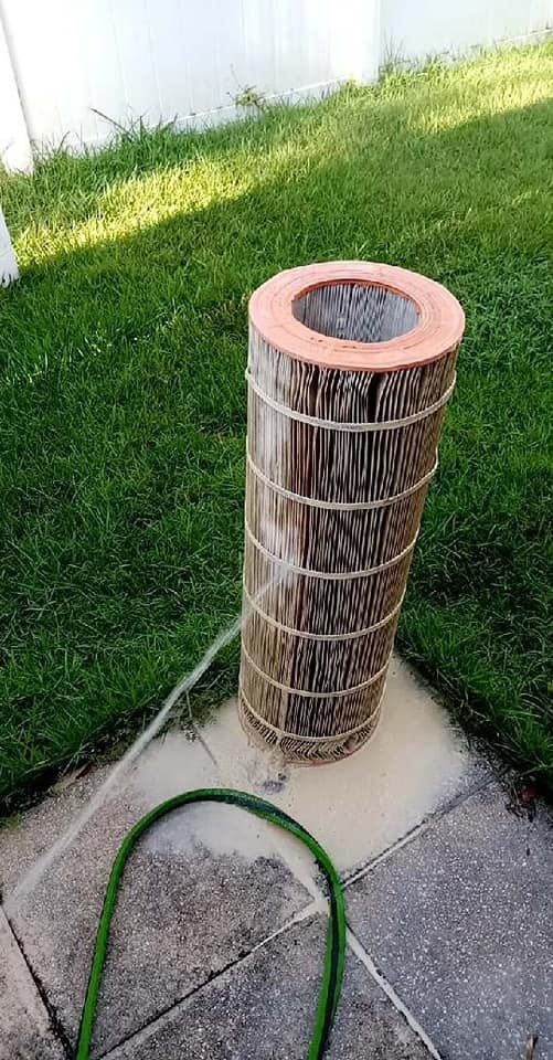 Air filter being rinsed with a hose on a concrete patio next to green grass.
