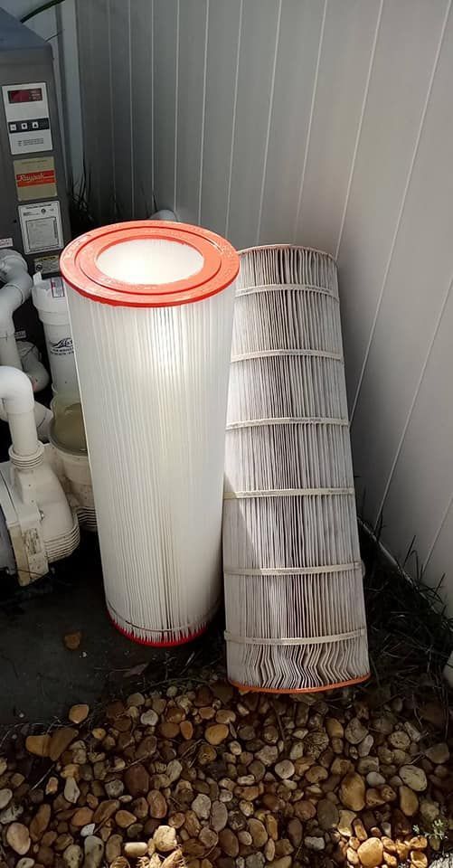 Two pool filters, one clean, one dirty, leaning against a wall next to rocks and pool equipment.