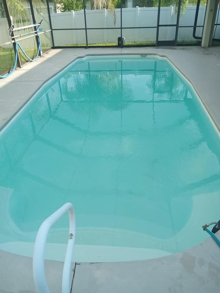 Swimming pool filled with turquoise water, surrounded by a concrete patio and a screened enclosure.
