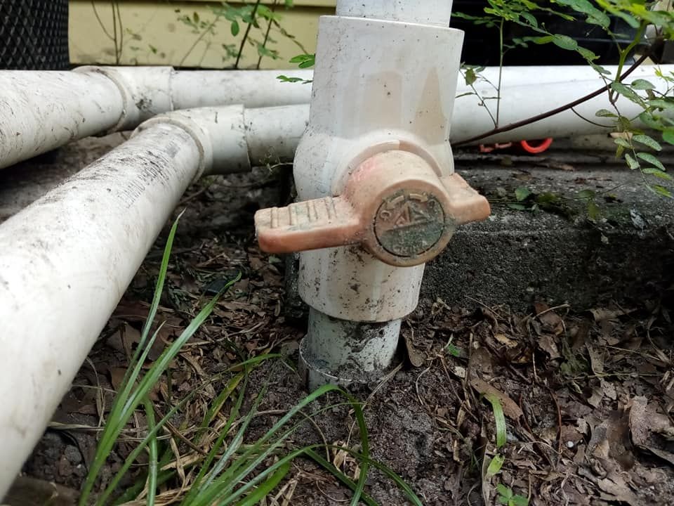 A PVC valve with a tan handle, set among white pipes and greenery.