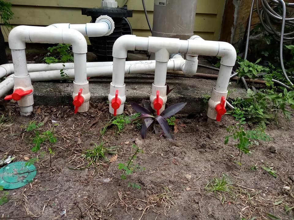 White PVC pipes with red valves, installed in a garden near pool equipment.
