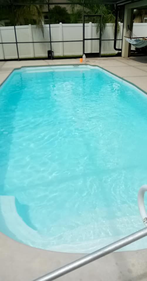 Pool with blue water and white steps, surrounded by concrete and a white fence.
