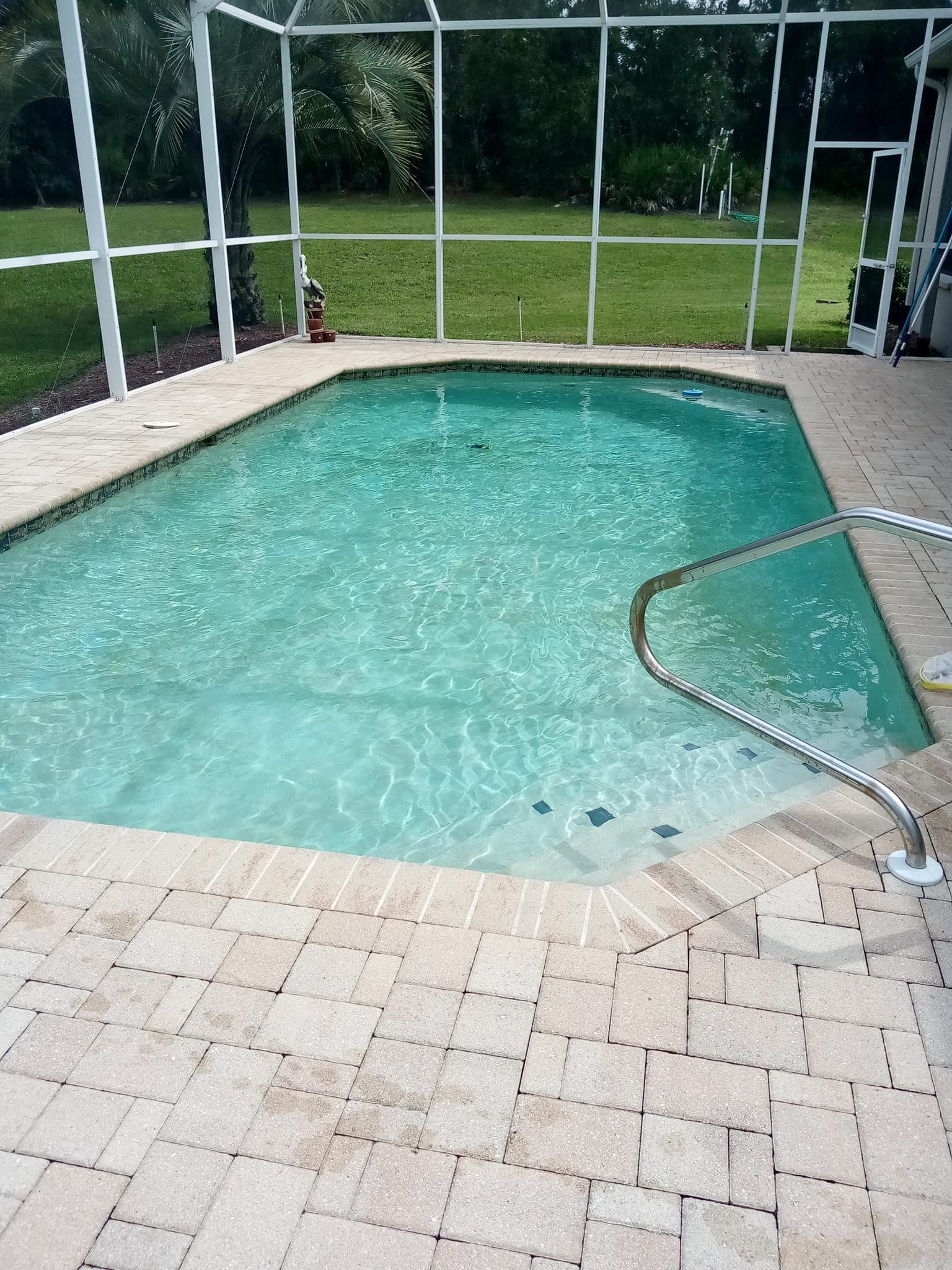 Pool with clear water, surrounded by tan brick and a white screen enclosure.