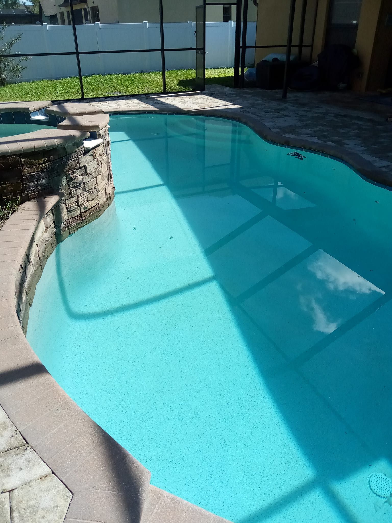 Blue swimming pool with dark coping and a screened enclosure.