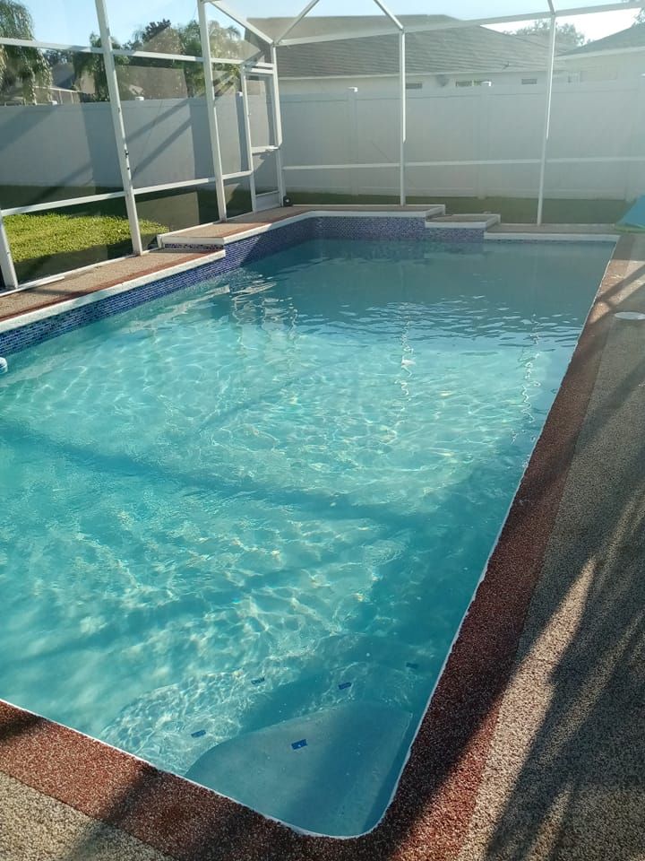 Rectangular swimming pool with clear water, surrounded by a patio and white screened enclosure.