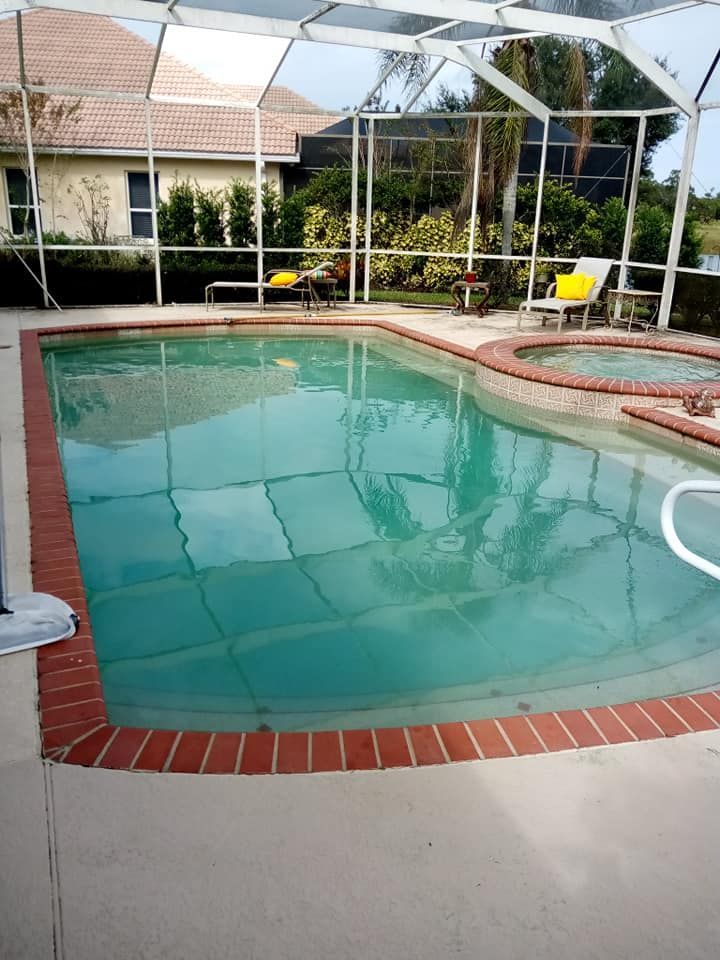 Swimming pool with brick edging, enclosed by a screen. Two lounge chairs are nearby.