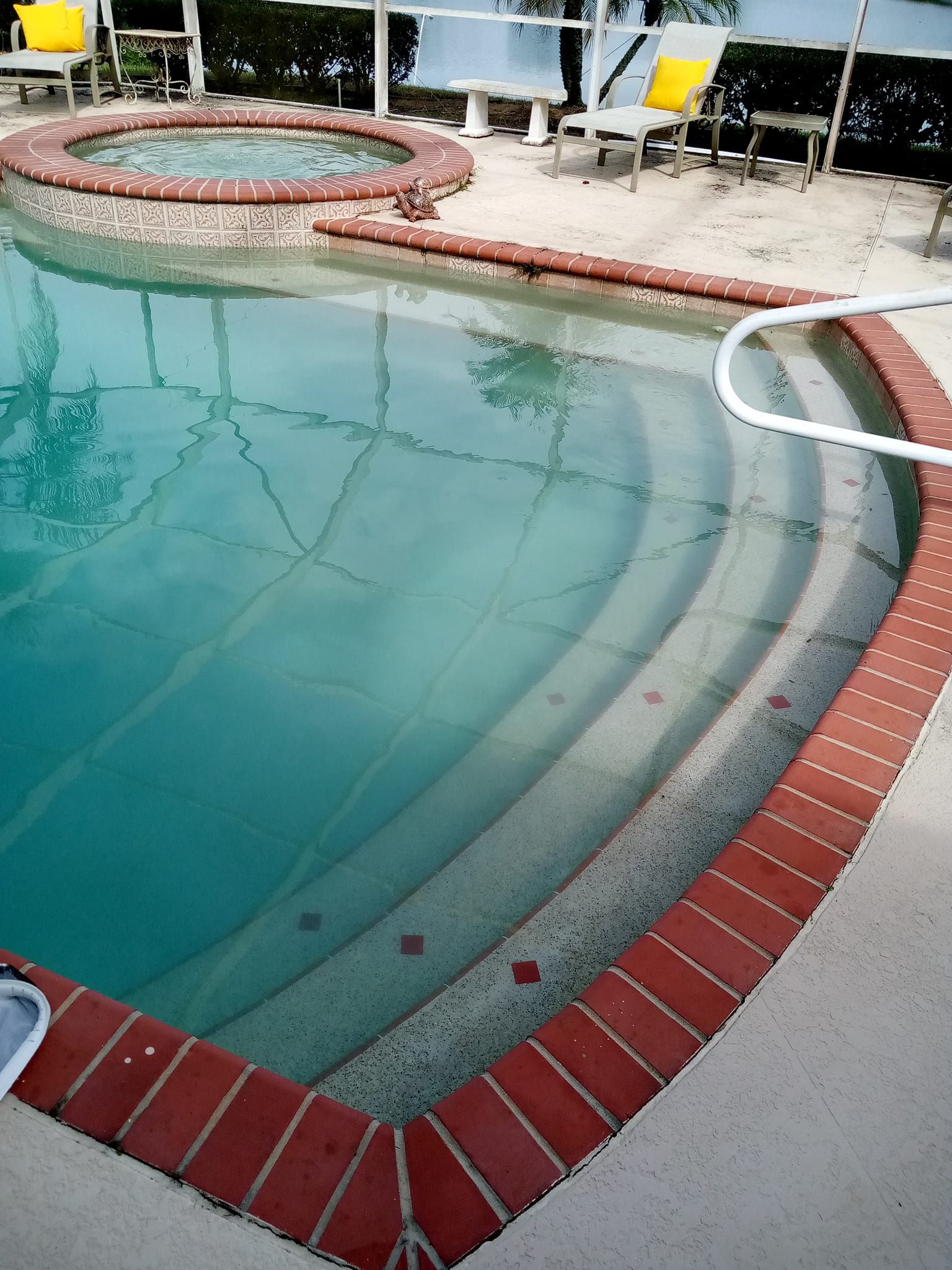 A pool with brick coping, steps, and a connected hot tub. The water is clear blue-green.