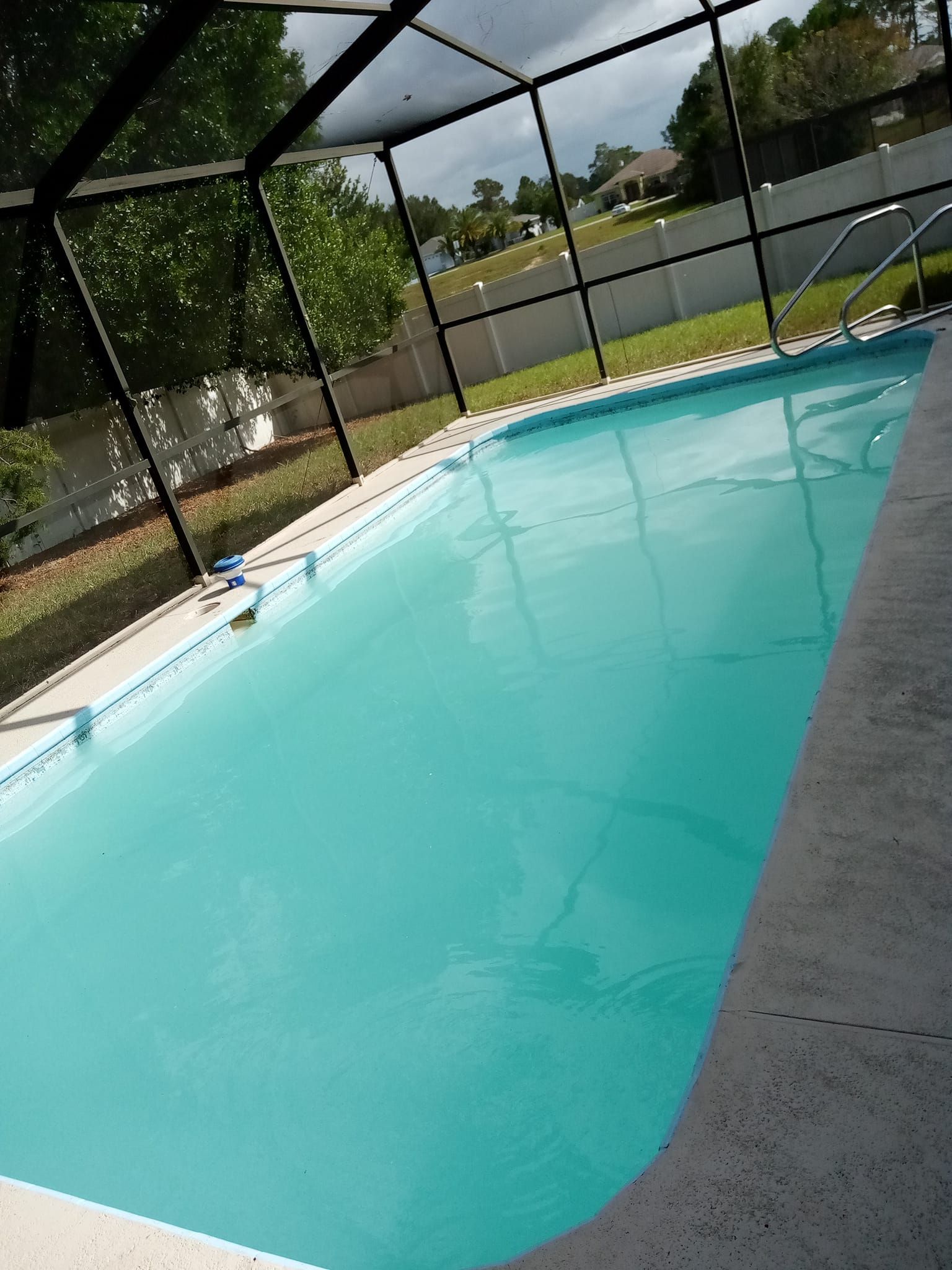 Swimming pool with turquoise water, screened enclosure, and grassy lawn in the background.