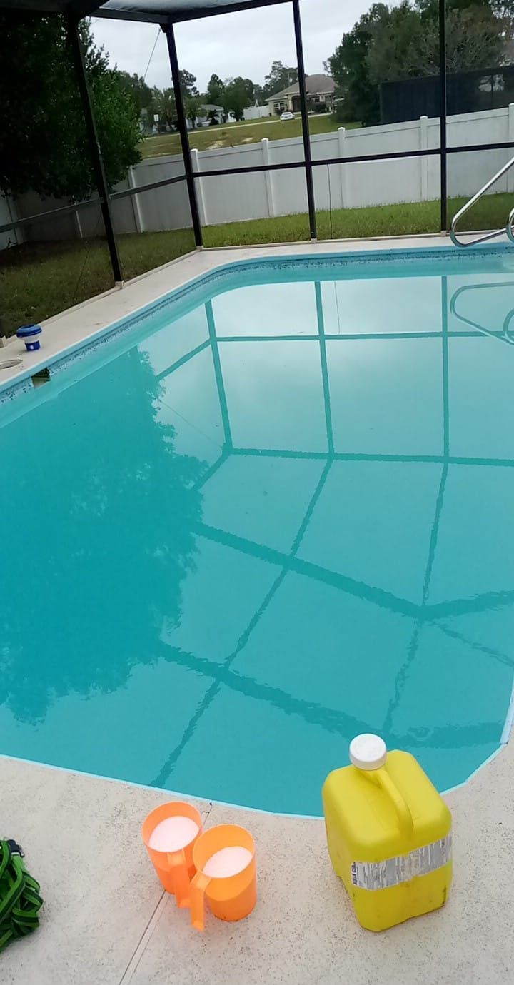 Swimming pool with turquoise water, surrounded by a concrete deck and screened enclosure.