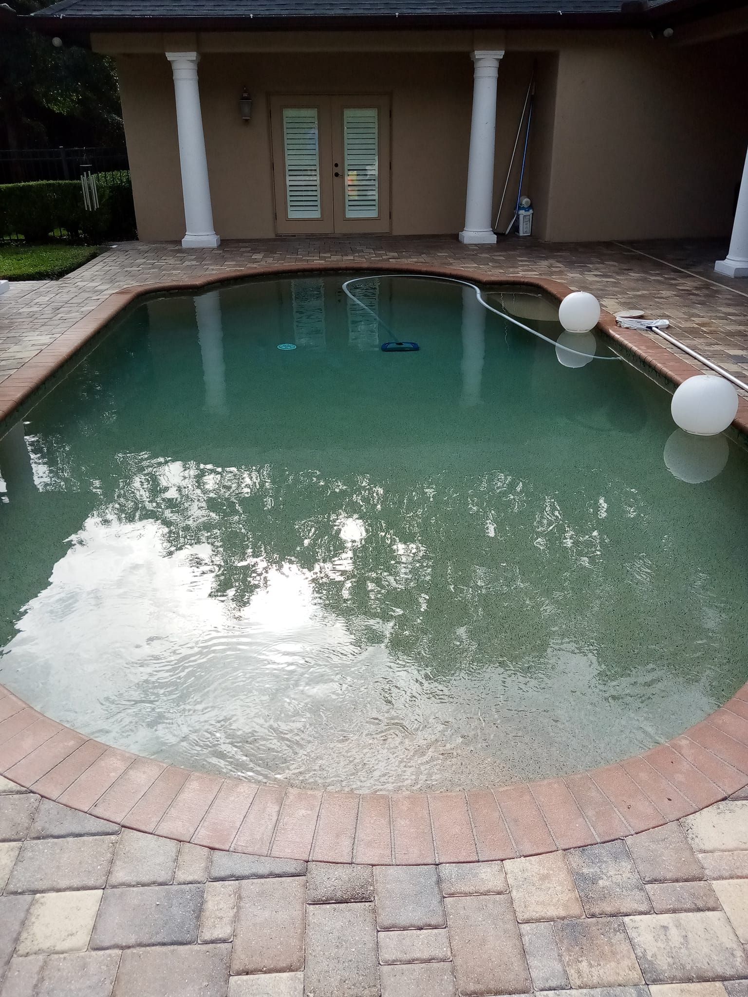 Swimming pool with brick border, patio, and two white decorative lights.