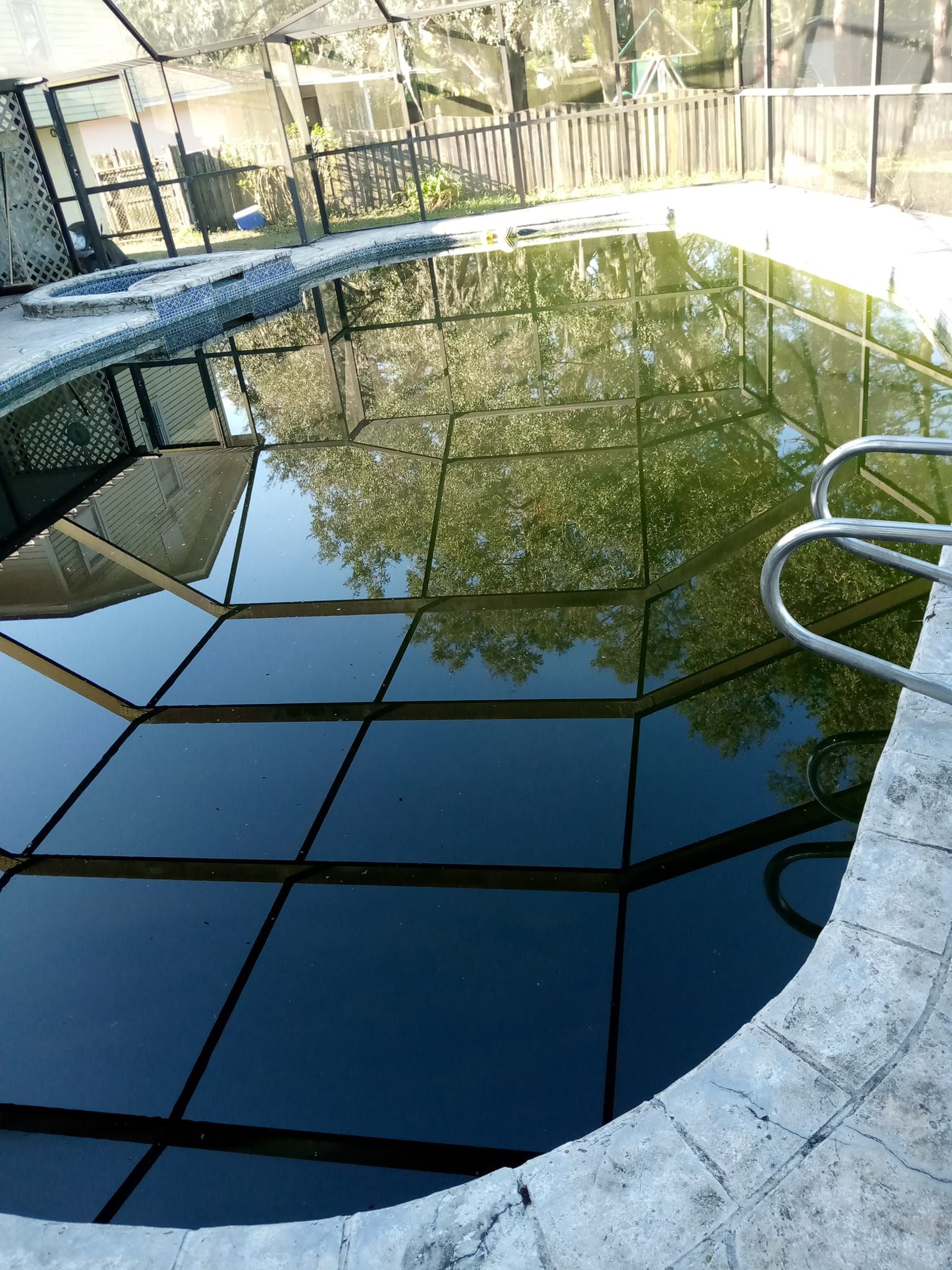 Green, murky pool with reflections, enclosed by a screen and stone edge.