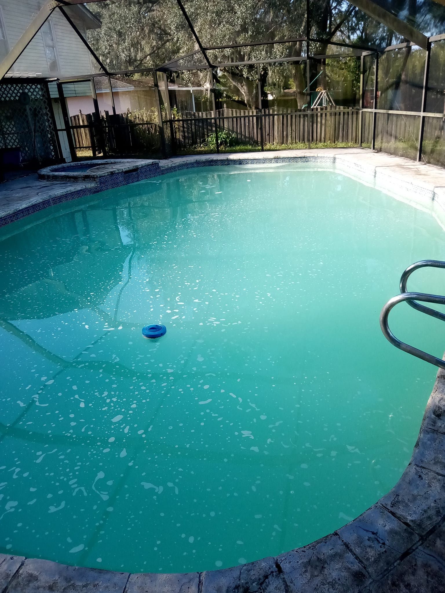 Pool with teal water, surrounded by stone and a screen enclosure. A blue cleaner floats.