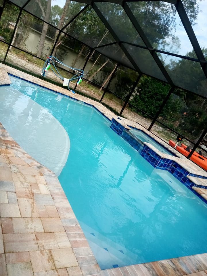 Swimming pool with turquoise water, beige tile, and a screened enclosure.