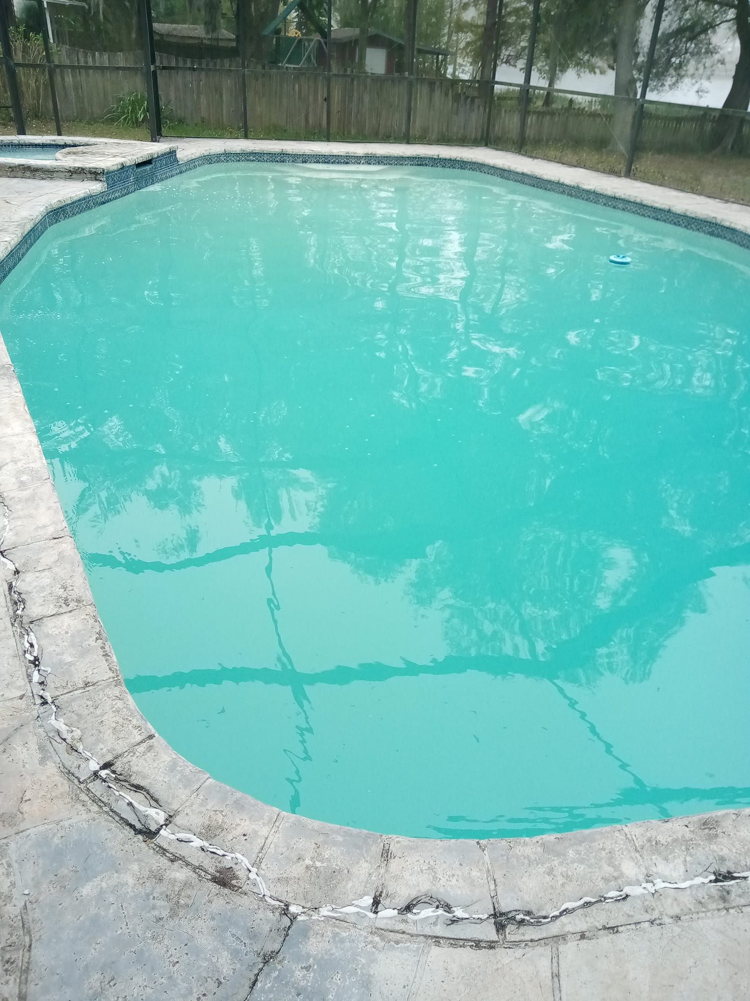 Swimming pool with turquoise water, surrounded by concrete and a fence.