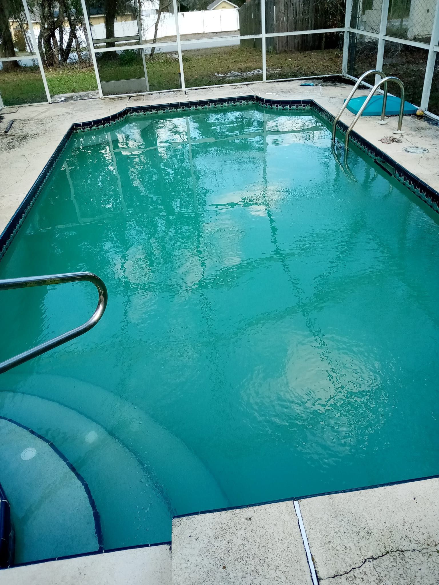 A rectangular swimming pool filled with turquoise water, with steps and a metal railing.
