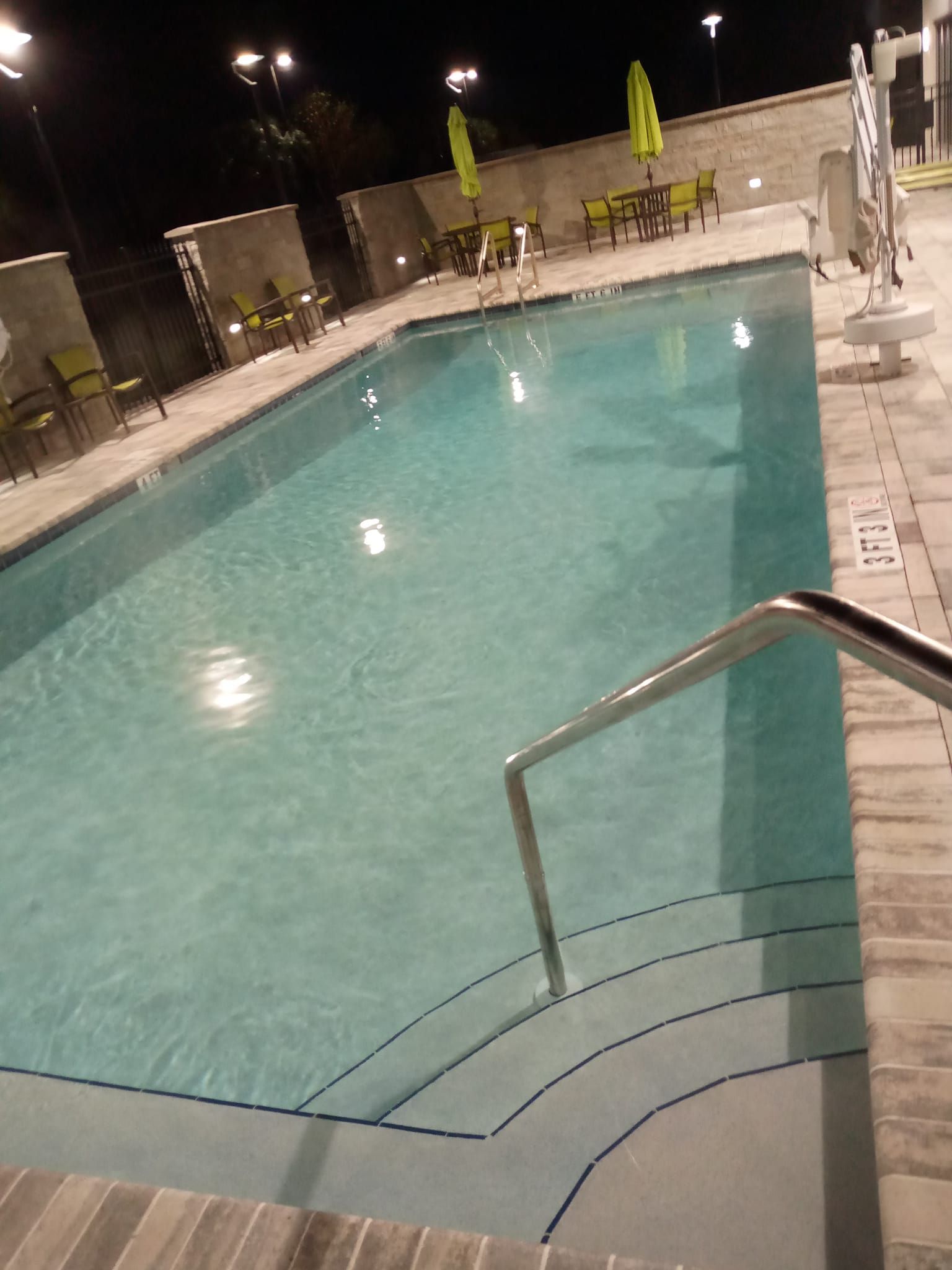 Pool at night with steps, handrail, and illuminated water. Patio furniture is visible.