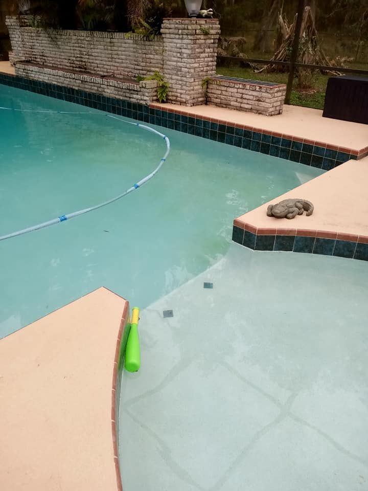 Pool with clear water, beige deck, and a sleeping cat. A pool cleaner floats in the water.