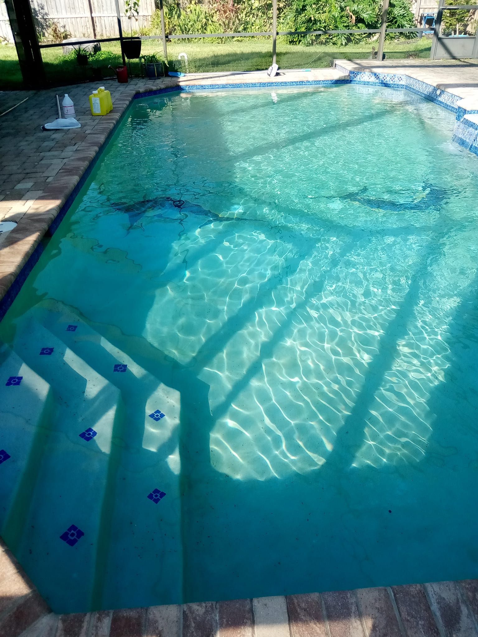 A rectangular swimming pool with clear turquoise water and steps. Sun casts shadows across the surface.