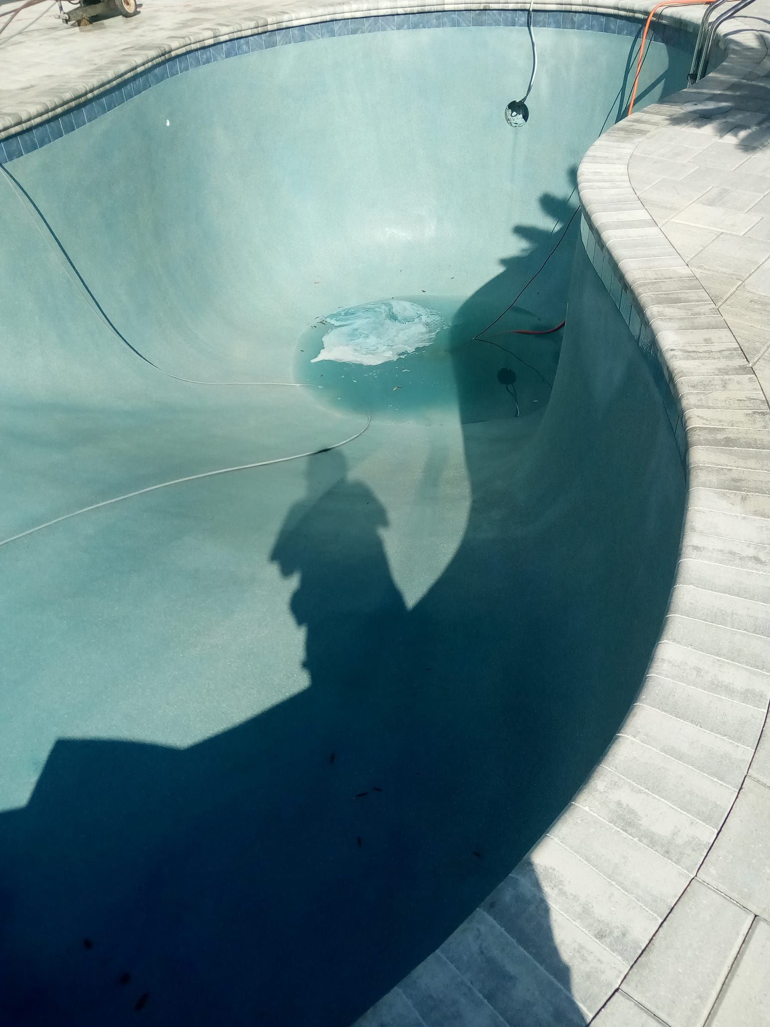 Empty turquoise swimming pool with shadow of person on surface. Stone coping.