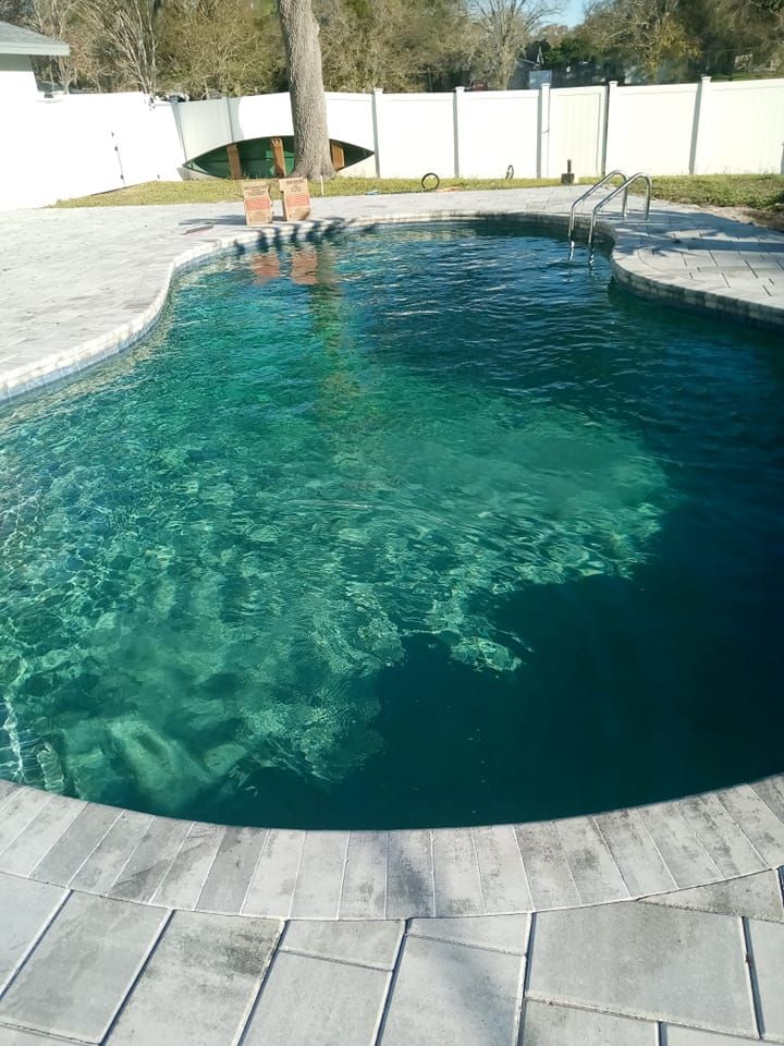 A swimming pool with clear turquoise water and a gray stone patio in a backyard.