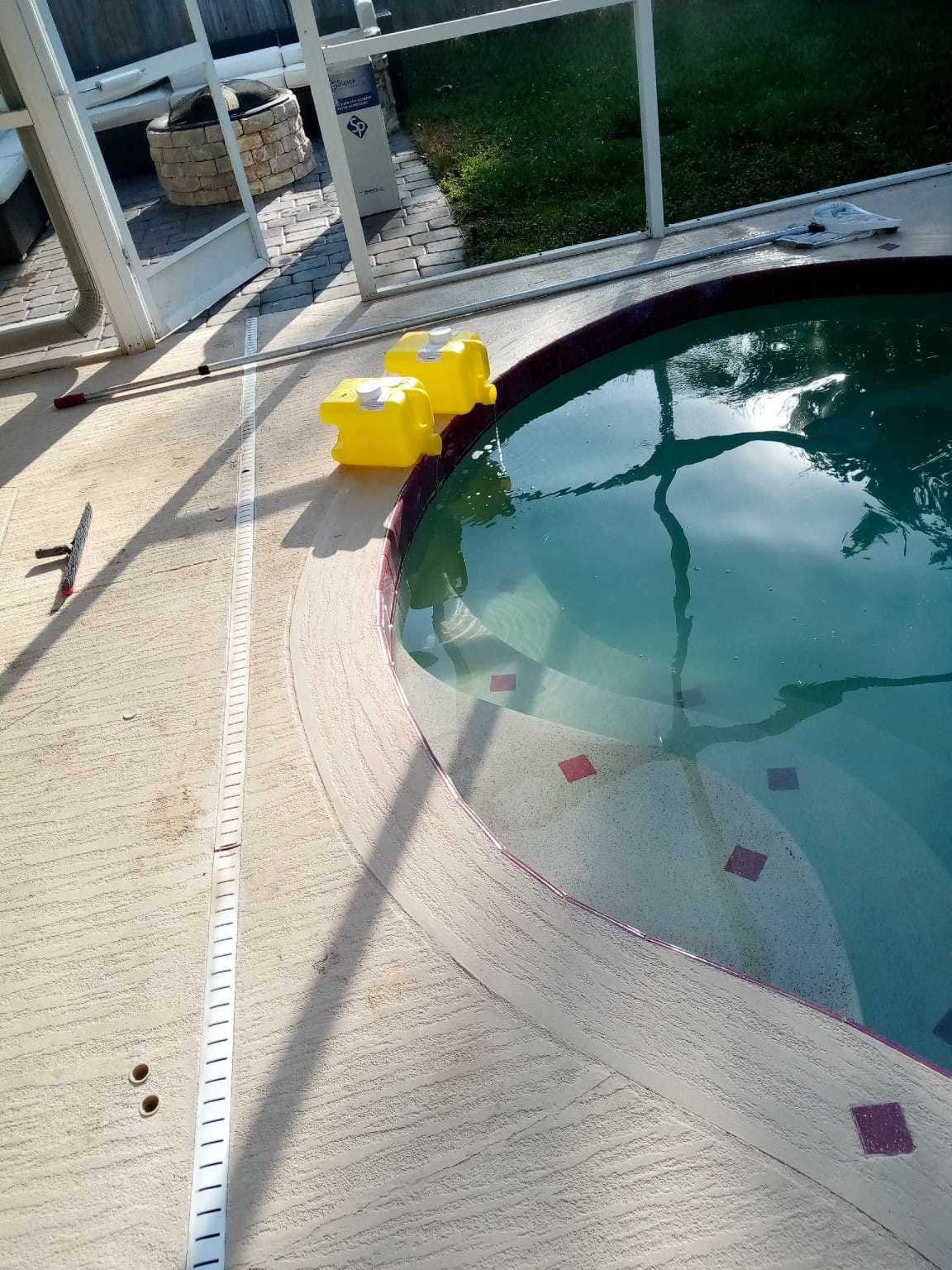 Pool with concrete surround, two yellow objects, and partial view of a screened enclosure.
