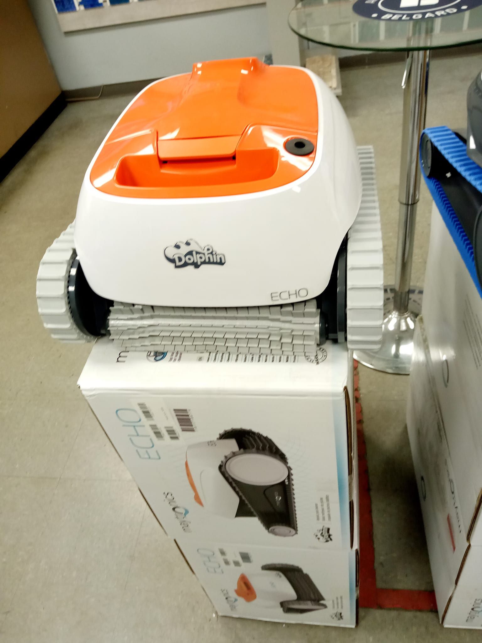 Orange and white robotic pool cleaner on display, perched on its product box.