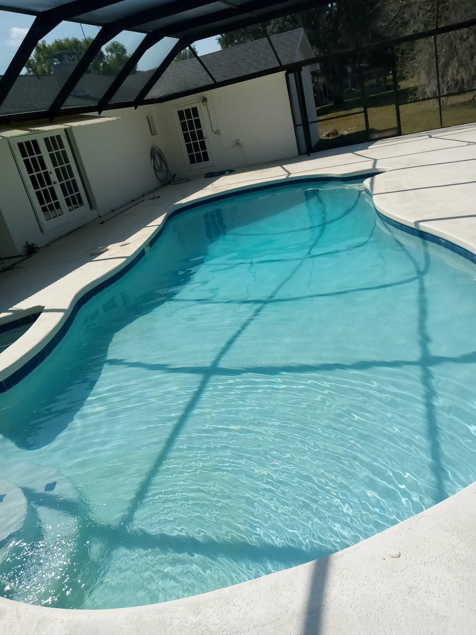 Swimming pool under a screened enclosure with blue water and light-colored decking.