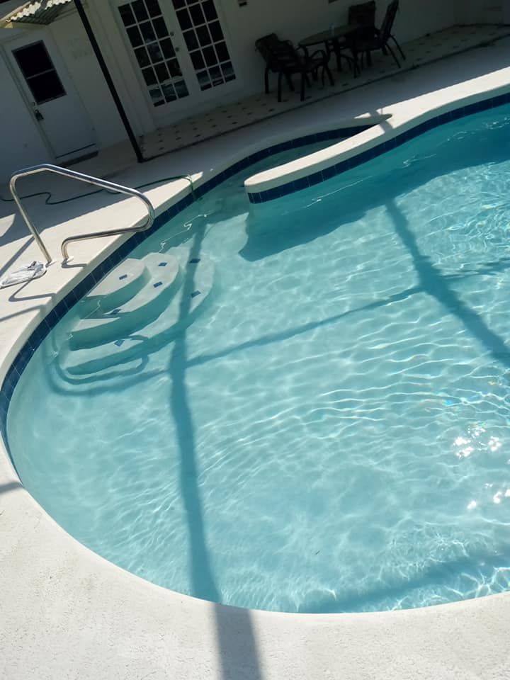 Swimming pool with blue water and steps, surrounded by white concrete.  Sunlight creates shadows on the water.