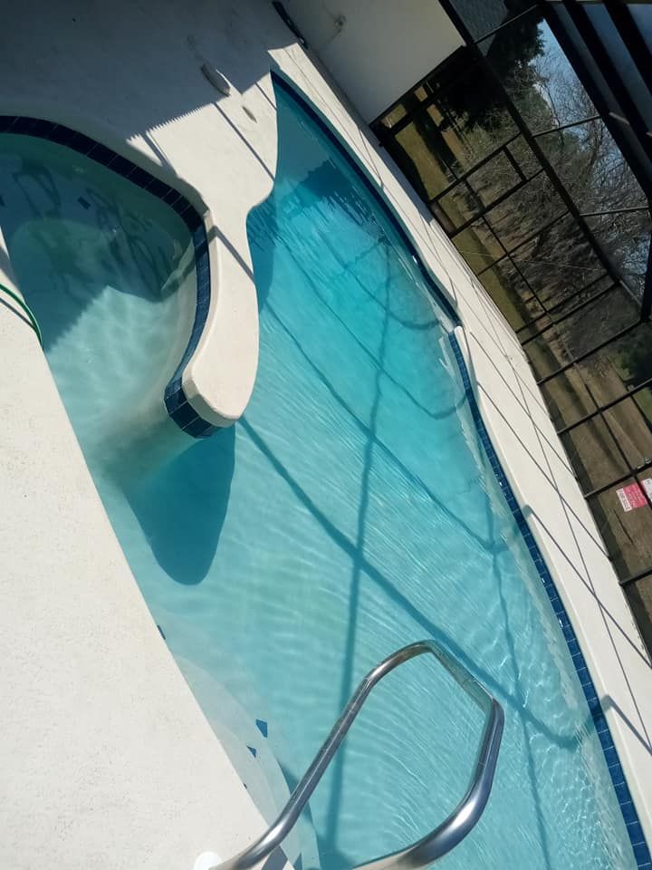 Indoor swimming pool with blue water and white tile, sunlight, and a metal handrail.