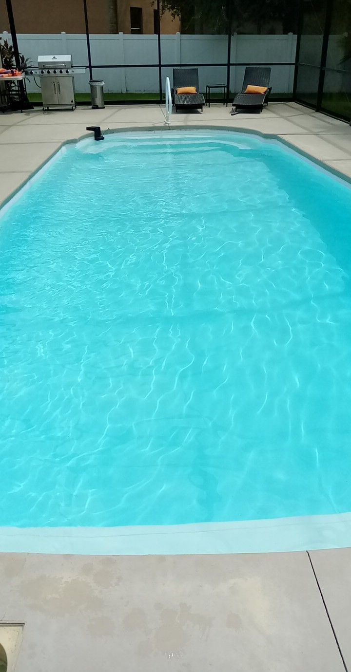 Blue swimming pool in a backyard, with lounge chairs and grill nearby.