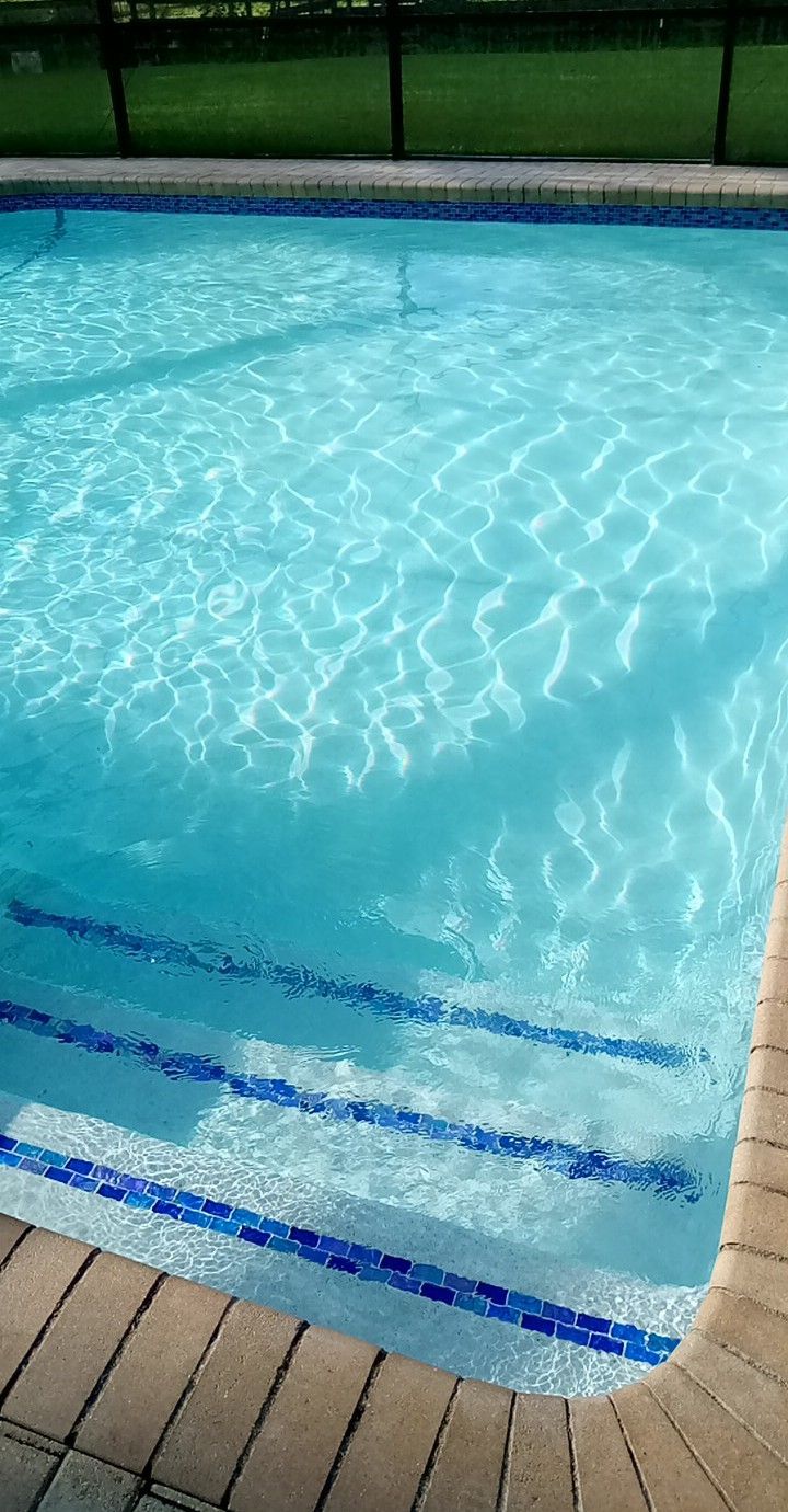 Pool with blue water and steps with blue tile detail; brick border, sunny setting.