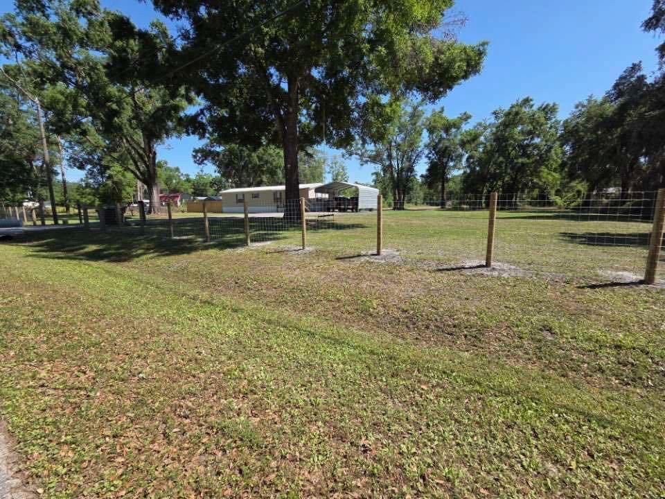 Grassy yard with trees, wooden fence, and a single-story building on a sunny day.