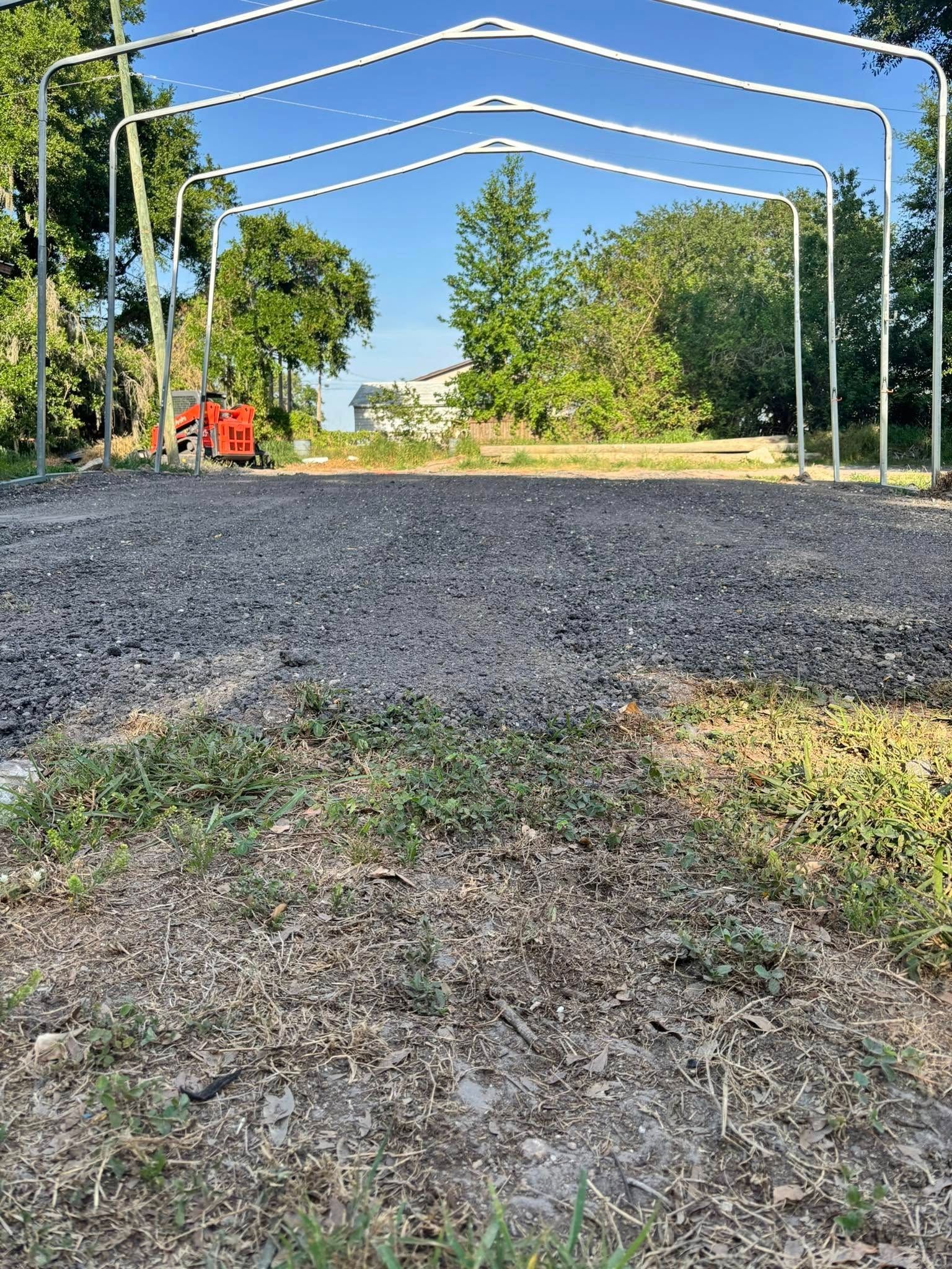White metal frame structure on gravel ground; trees and blue sky background.