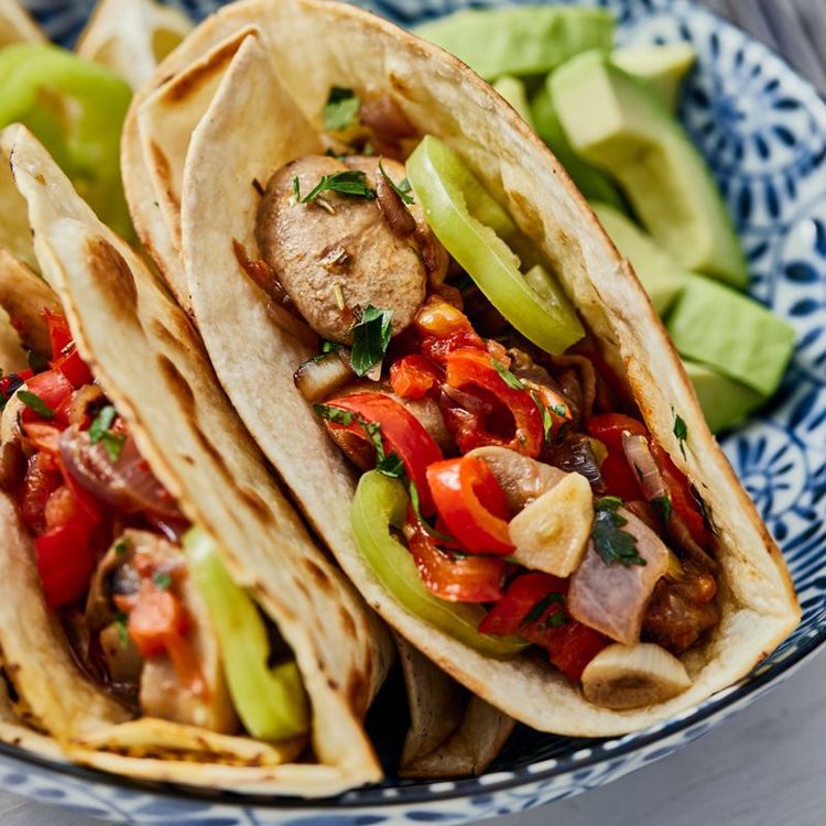 Tacos with grilled chicken, peppers, and avocado on a blue plate