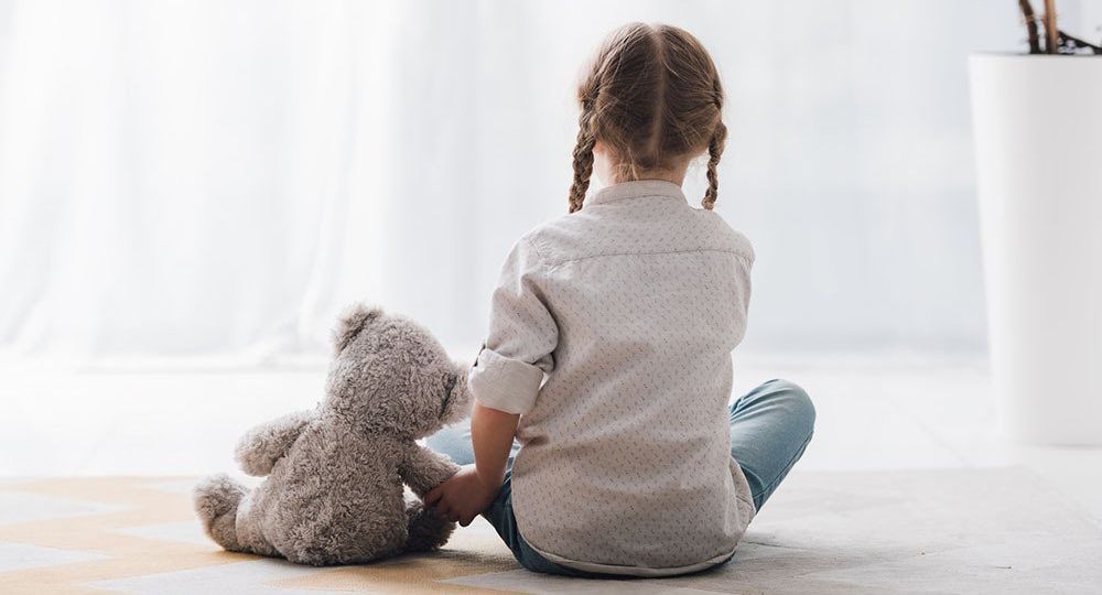 a little girl sits on the floor holding a teddy bear