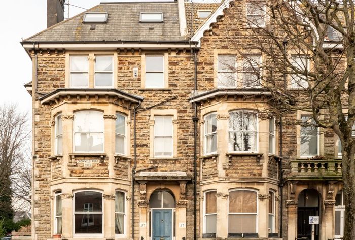 Stone townhouse facade with bay windows and dormers, fronted by bare trees