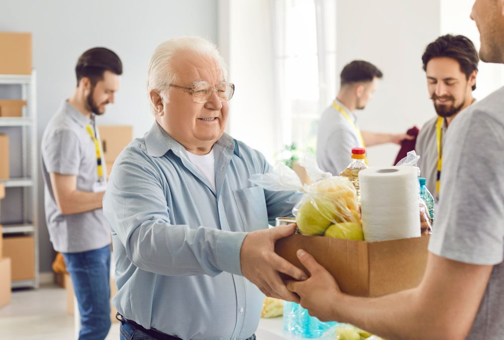 Volunteers passing a box of groceries in a bright kitchen