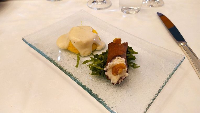 Due antipasti gourmet serviti su un piatto di vetro con salsa, su una tovaglia bianca.