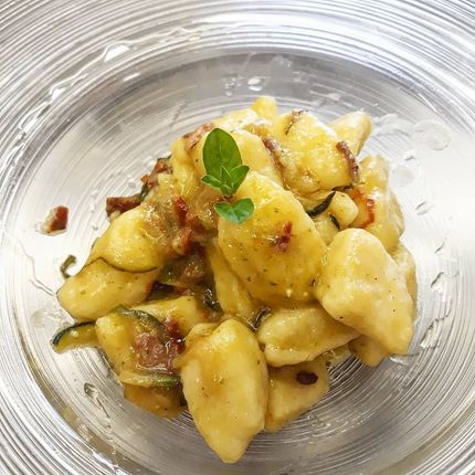 Gnocchi in una ciotola di vetro, conditi con erbe aromatiche e una salsa leggera.