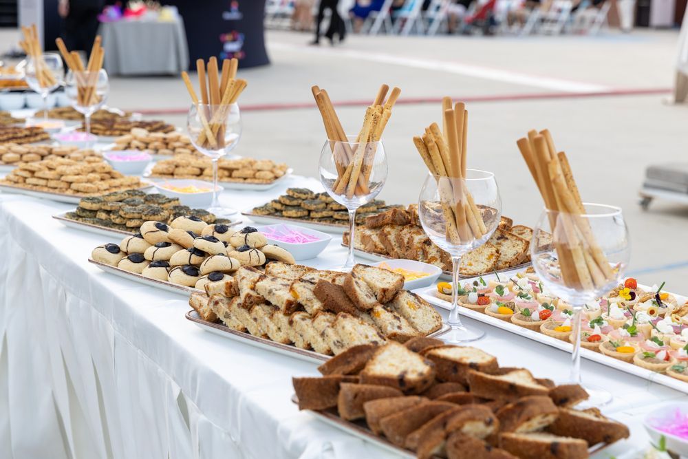 Tavolo da buffet con pane assortito, cracker e grissini disposti in ciotole e vassoi trasparenti.