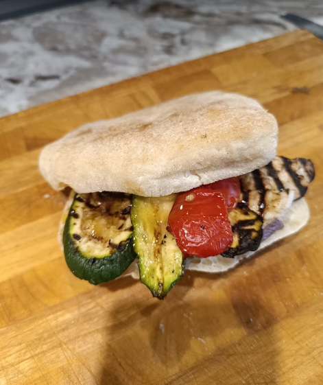 Panino con verdure grigliate in una morbida pita su un tagliere di legno.