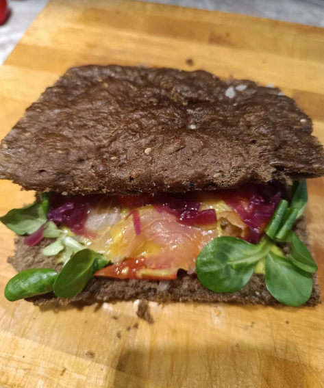 Panino rustico con pane integrale, verdure a foglia verde e cipolla rossa su un tagliere di legno.