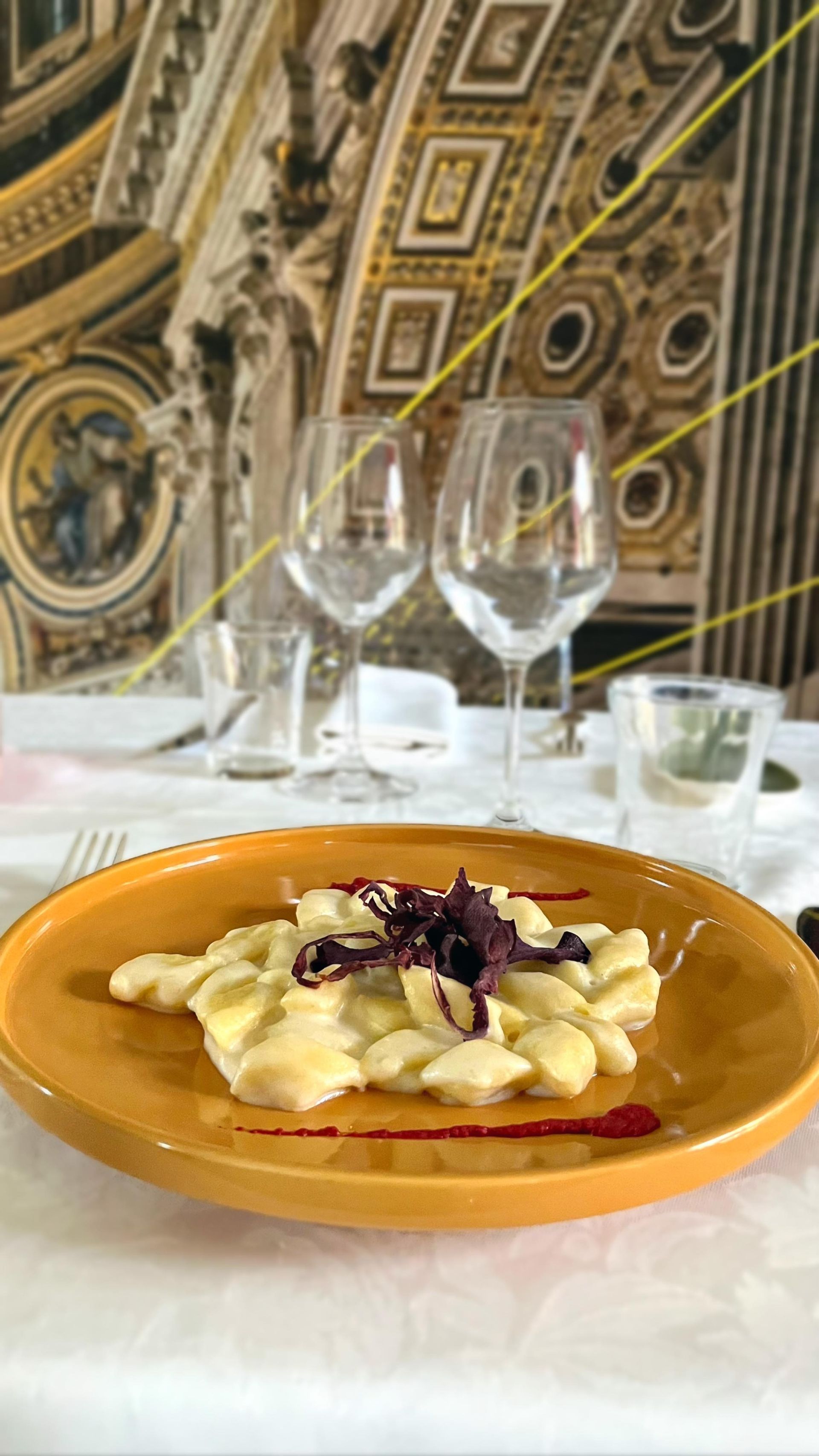 Un piatto di pasta arancione con guarnizione viola su un tavolo bianco in un ristorante sfarzoso.